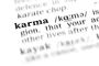 Nahaufnahme einer aufgeschlagenen Wörterbuchseite, die sich auf das hervorgehobene Wort „Karma“ konzentriert. Das Wort ist fett gedruckt und zeigt die Lautschrift „/ˈkɑːrmə/“. Ein Teil der Definition ist sichtbar. Der schwarze Text hebt sich deutlich vom unscharfen Hintergrund ab. Dieses Bild symbolisiert die tiefe Bedeutung von Karma und seine Einflussnahme auf die Gesellschaft.