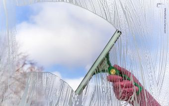 Rückblick auf den März 2025: Eine Hand wischt mit einem Abzieher ein Fenster sauber und gibt den Blick auf einen wolkigen Himmel und Äste frei. Seifenreste und Streifen bedecken den Rest des Fensters. Dies steht symbolisch für klare Sicht und Frühjahrsputz im Business.