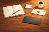 Symbolbild f&uuml;r Notion-KI mit Google verbinden: Heller Holztisch mit offenem Notizbuch, Bleistift, Kaffeetasse, Umschlag, Kalender, Papierklammern