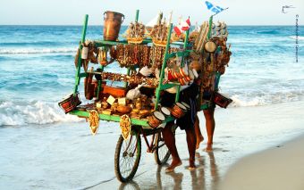 Ein Verkäufer schiebt sein Fahrrad mit einem überfüllten Verkaufsgestell am menschenleeren Strand entlang. Das ild steht symbolisch dafür, dass ein Bauchladen als Onlinebusiness-Modell ungeeignet ist.